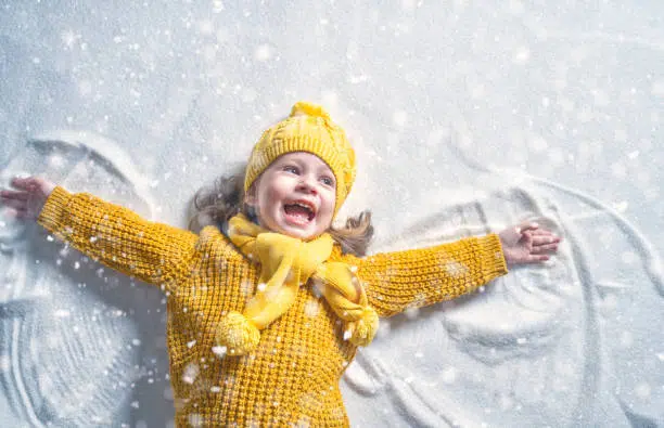 Happy child girl playing on a winter walk in nature. Kid making snow angel.